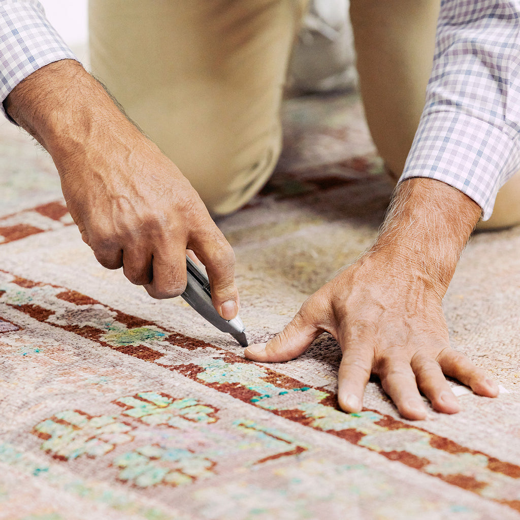 Skilled craftsman meticulously trims patterned carpet using a utility knife.
