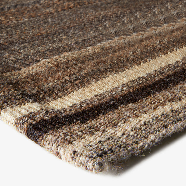 Close-up shot of a textured, striped woven rug in earth tones.