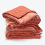 Neatly folded, terracotta quilt with textured stitching and plush appearance.