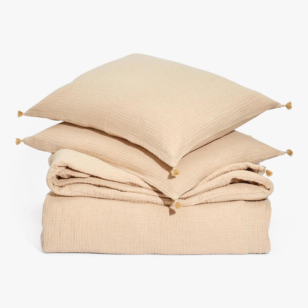 Neutral sandy-beige bed linens with tassel pillows on canvas-like texture.