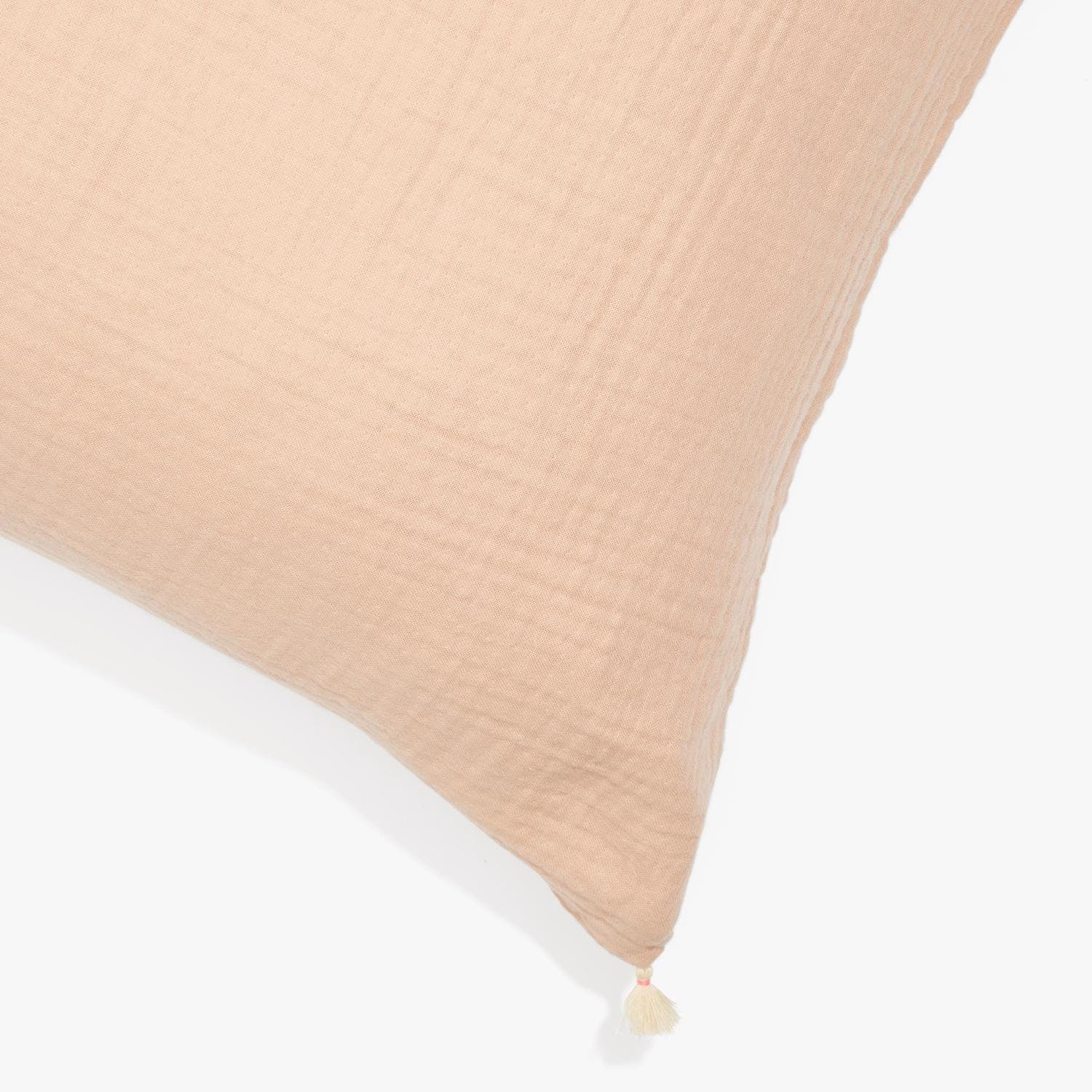 Blush pink linen cushion with crinkled texture and decorative tassel.