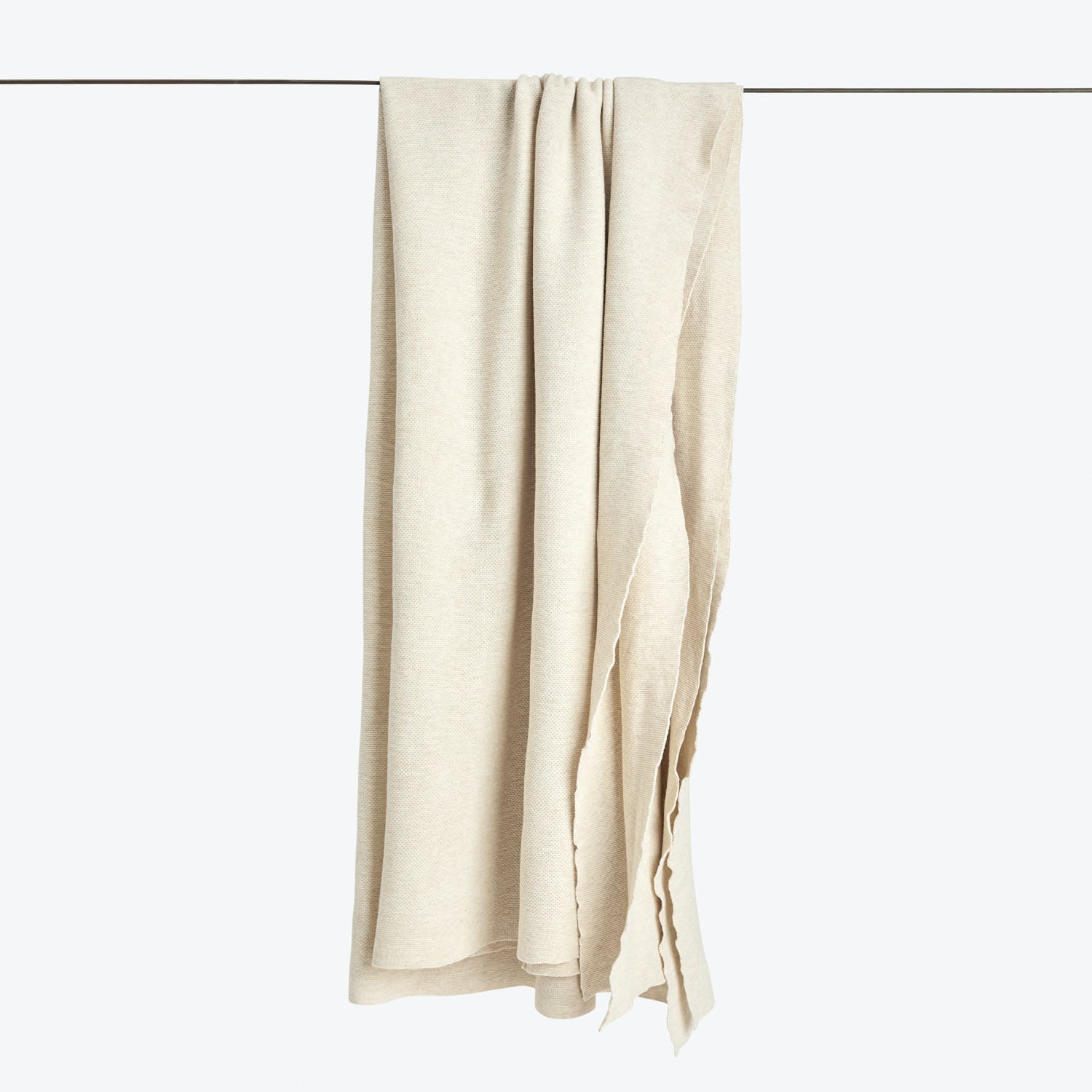 Beige fabric curtain folded on a rod against white background.