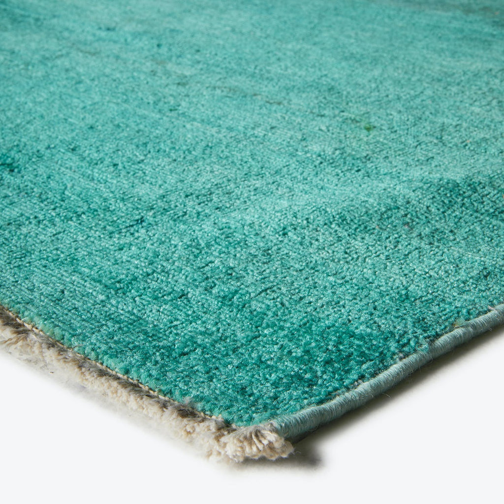 Close-up of teal rug with plush pile and bound edge.