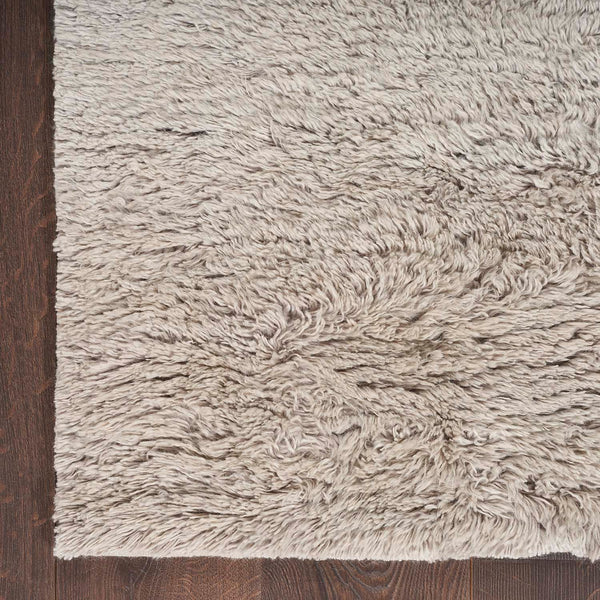 Close-up of a plush, shaggy rug in light beige/grey color, contrasting with a dark wooden floor.