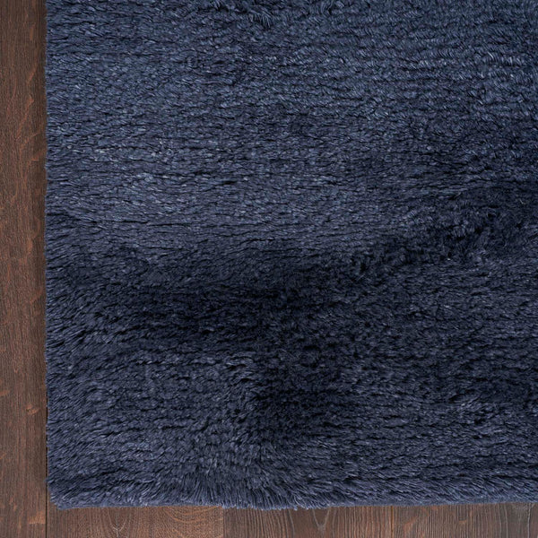 A close-up of a dark shaggy rug on a wooden floor.