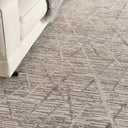 Close-up of a textured carpet with geometric diamond pattern, complemented by a modern sofa and cozy gray blanket.