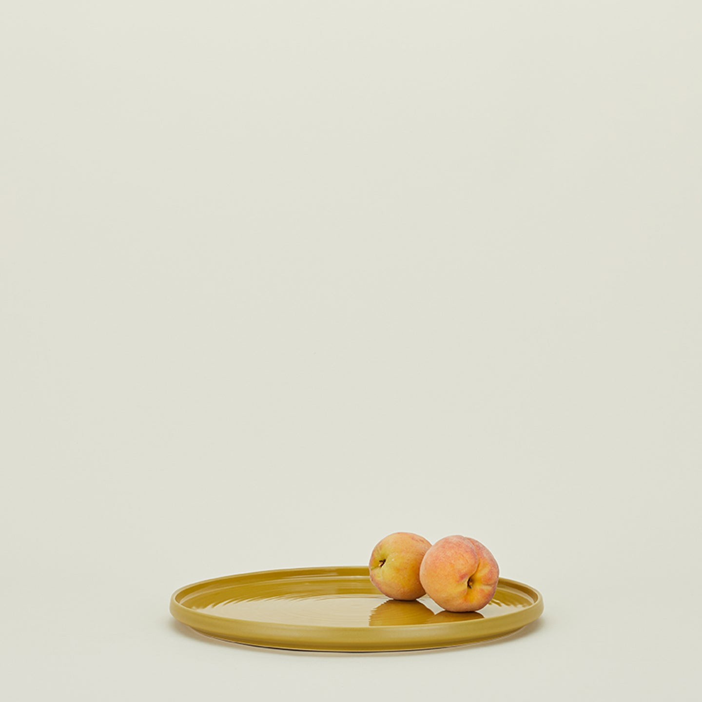 Minimalist composition featuring two ripe peaches on an olive plate.