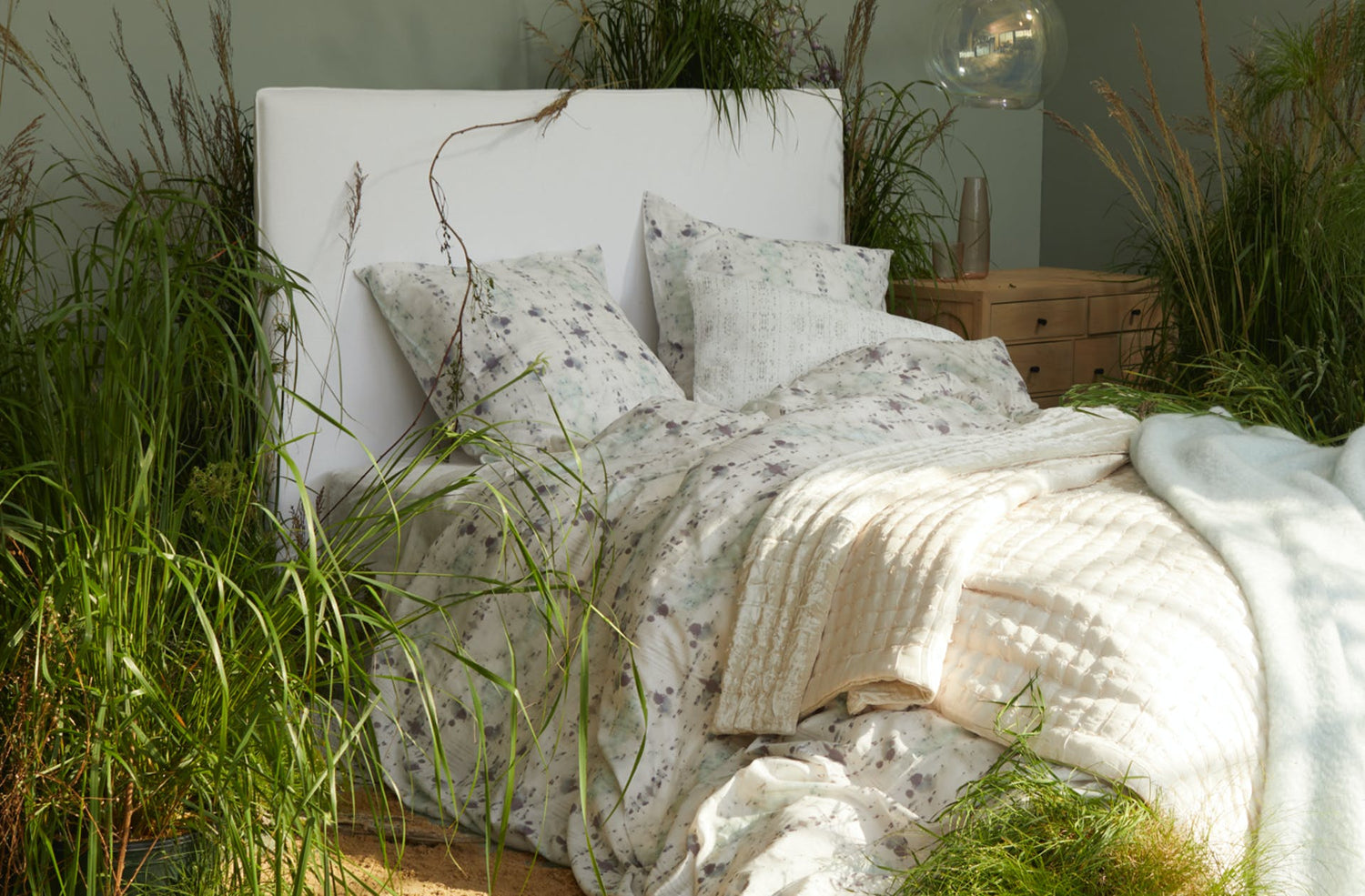 White bed surrounded by green plants with white floral bedding set and