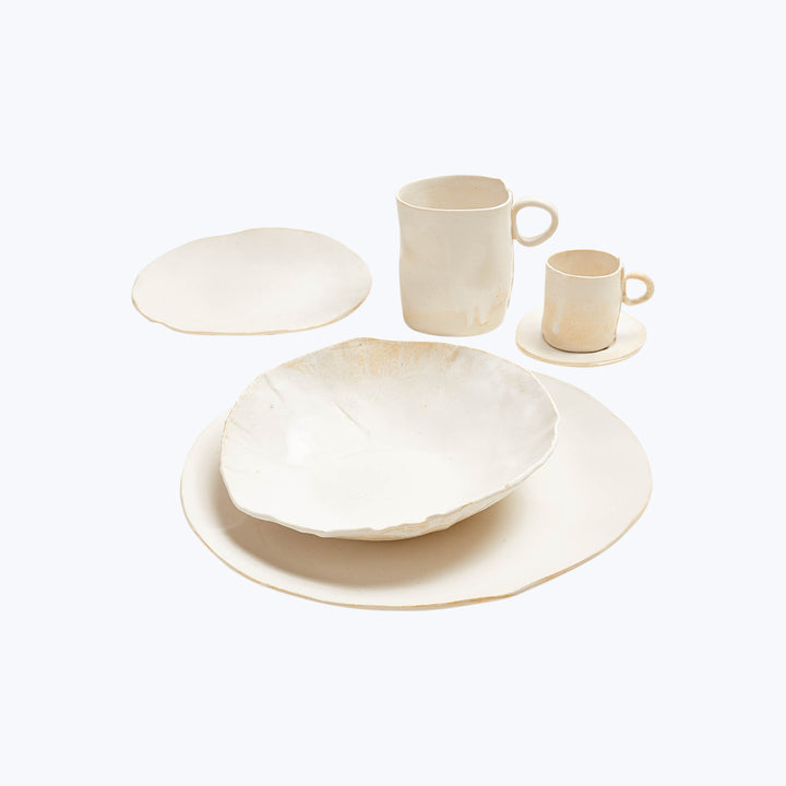 Handmade ceramic dinnerware set with rustic charm against white background.