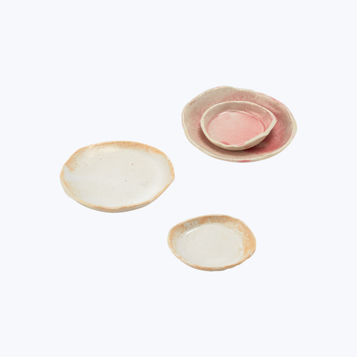 Handmade ceramic dishes in pink, white, and brown hues arranged diagonally.