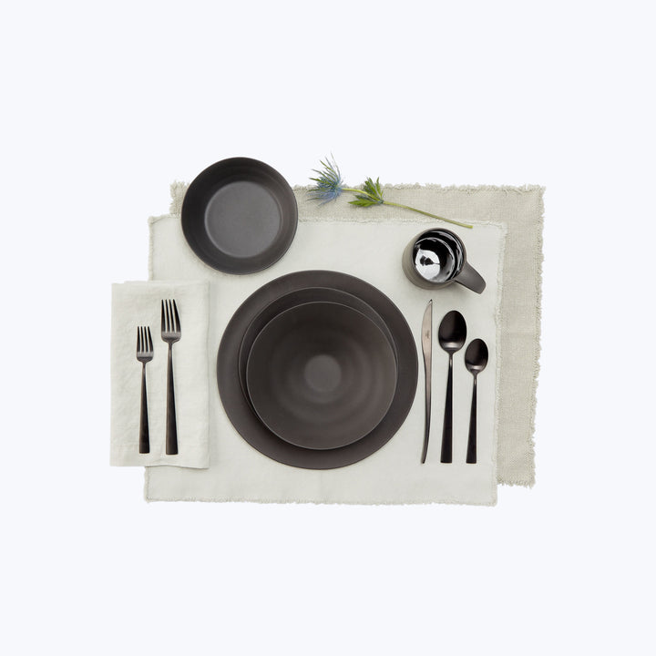 Modern black table setting on light linen with green plant.