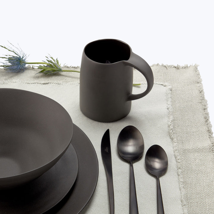 Modern, minimalist table setting with black tableware and blue flowers.