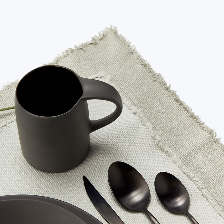 Modern monochromatic coffee set: mug, spoons, knife, plate, placemat.