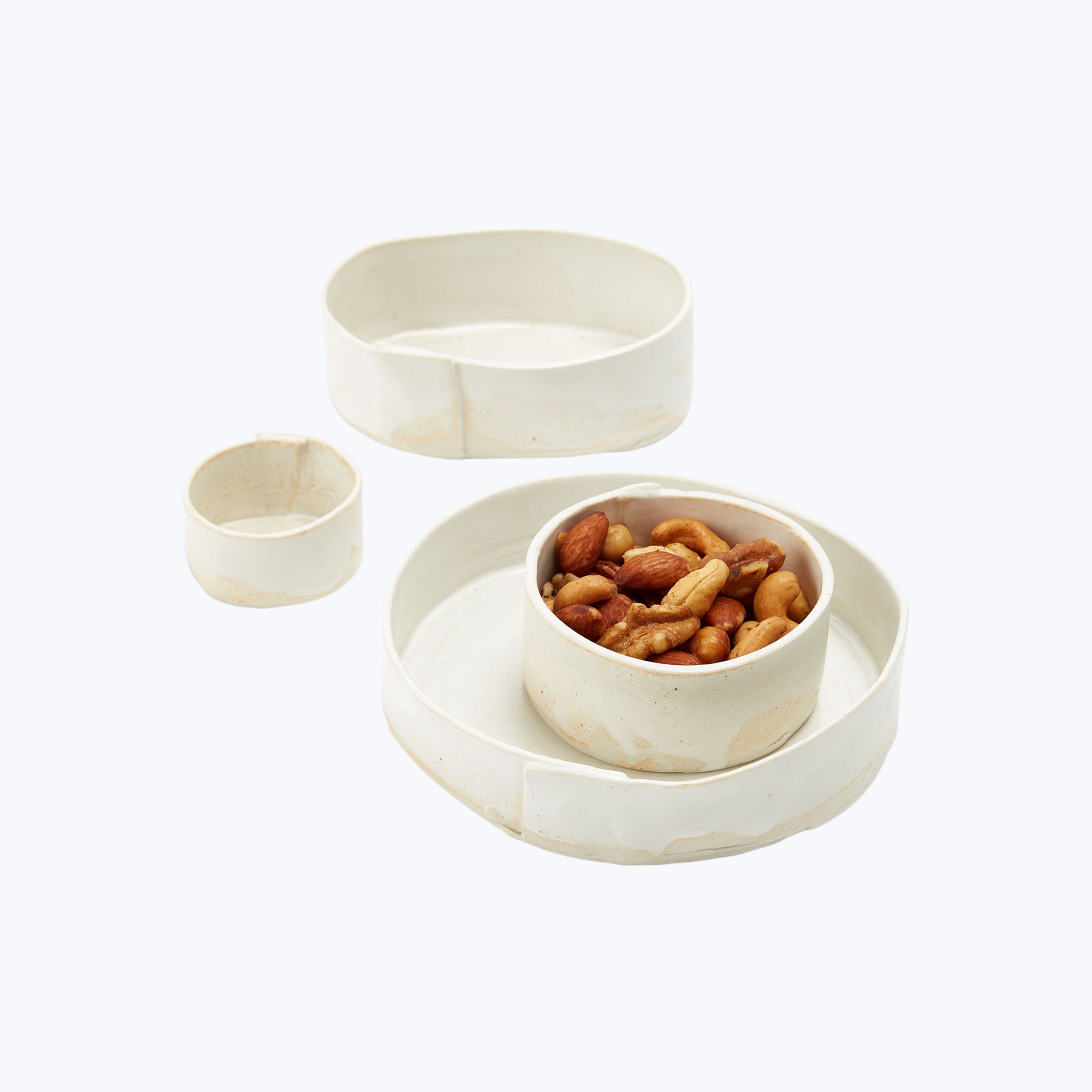 Three-piece serving dish set with mixed nuts on white background.