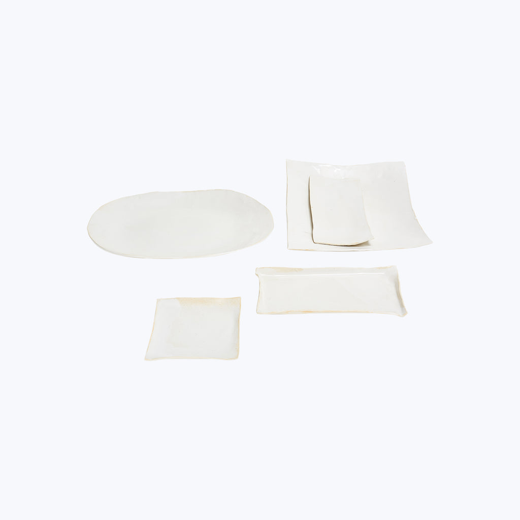 Modern, artisanal collection of white ceramic tableware on plain background.