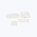 Modern, artisanal collection of white ceramic tableware on plain background.