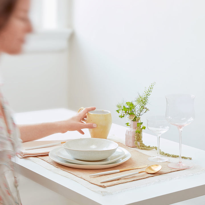 Elegant table setting with ceramic mug, wine glasses, and greenery.