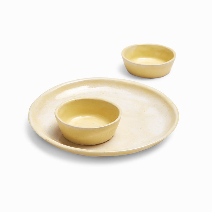 Minimalist ceramic tableware set in pale yellow on white background.