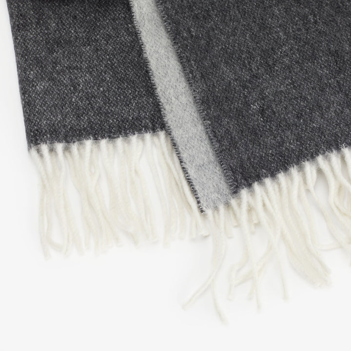Gradient woven textile blanket with fringed edge in gray hues.