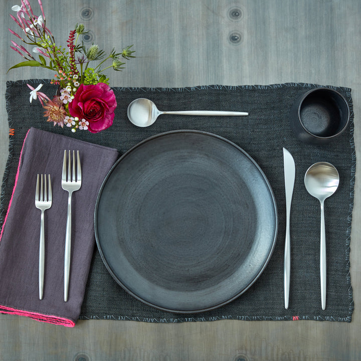 Neatly arranged table setting with modern silverware, dark gray placemat.