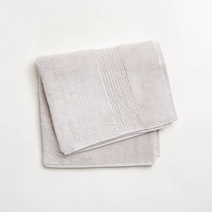 Neatly folded beige towel with decorative border on white background.