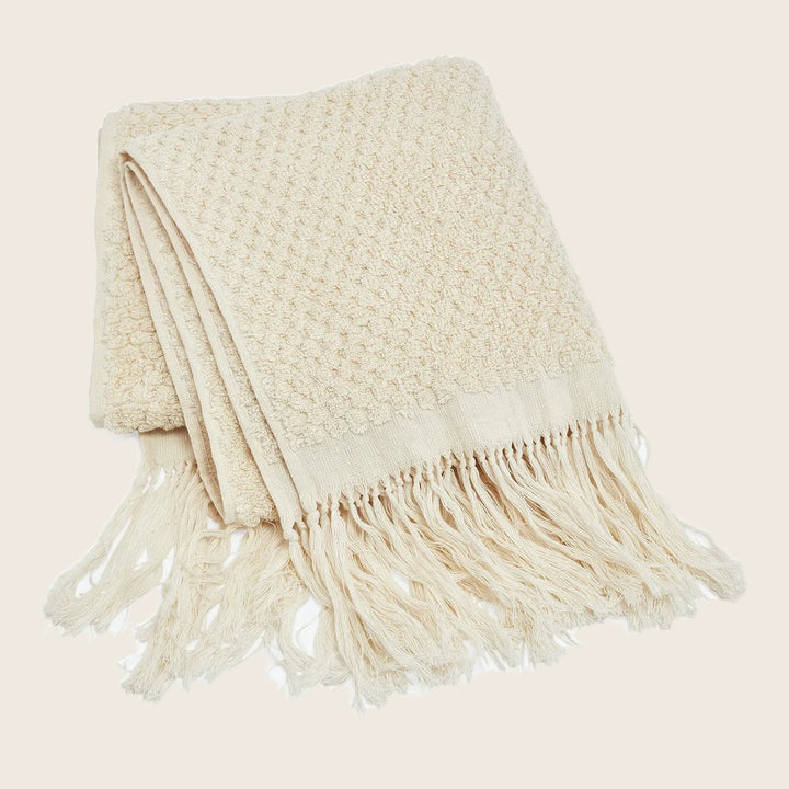 Cream throw blanket with textured pattern and fringe detailing folded neatly.