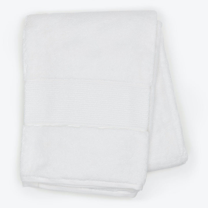 Soft white bath towel with decorative band on white background.