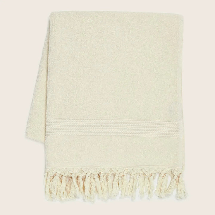 Folded towel with decorative band and tassels on plain background.
