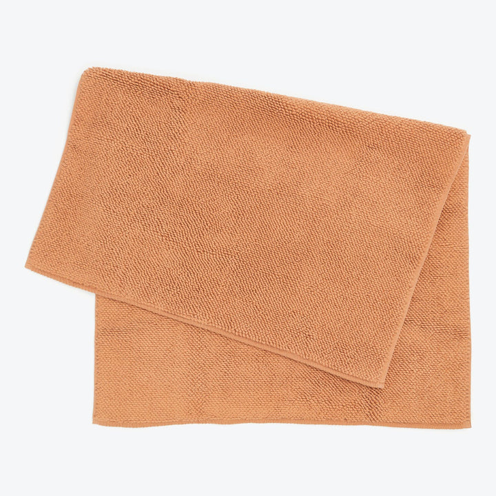 Two terracotta-colored terrycloth towels folded on white background.