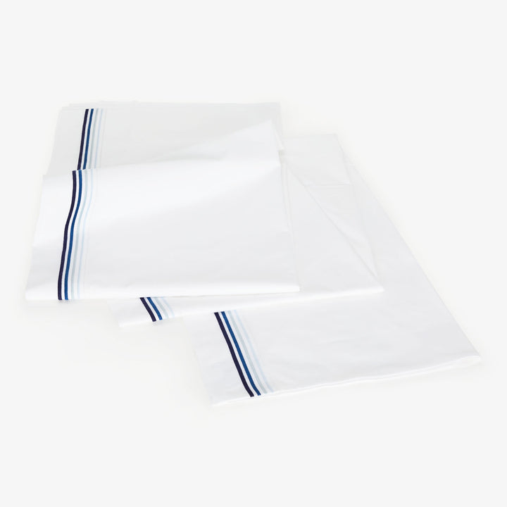 Crisp white bed sheets with navy blue stripe for decor.
