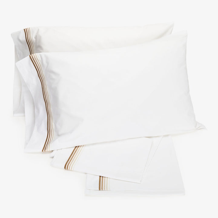 Crisp white bed linens with tan striped detail folded neatly.