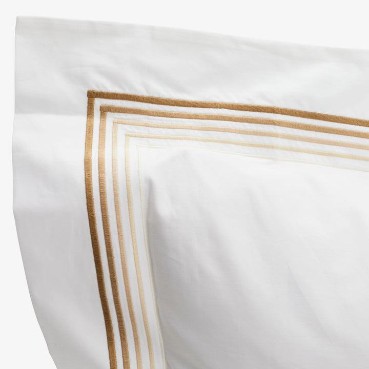 Elegant white fabric with golden-brown embroidery trim for luxury bedding.