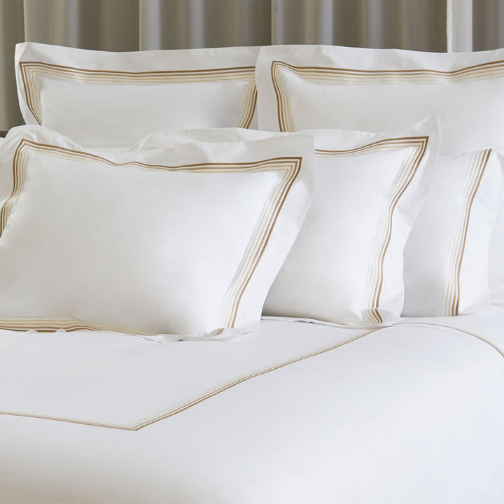 Luxurious white bedding with elegant gold striped pillows, high-end bedroom.