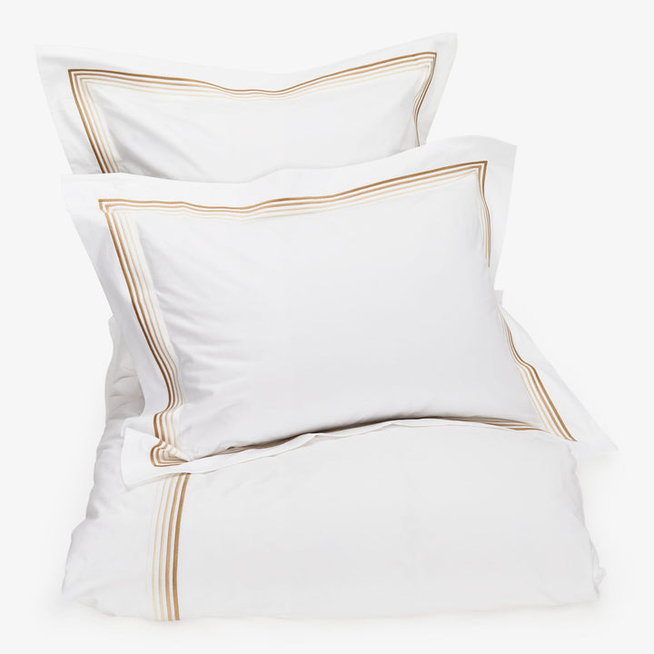 Elegant white bedding set with golden-brown embroidered trim, minimalist design.