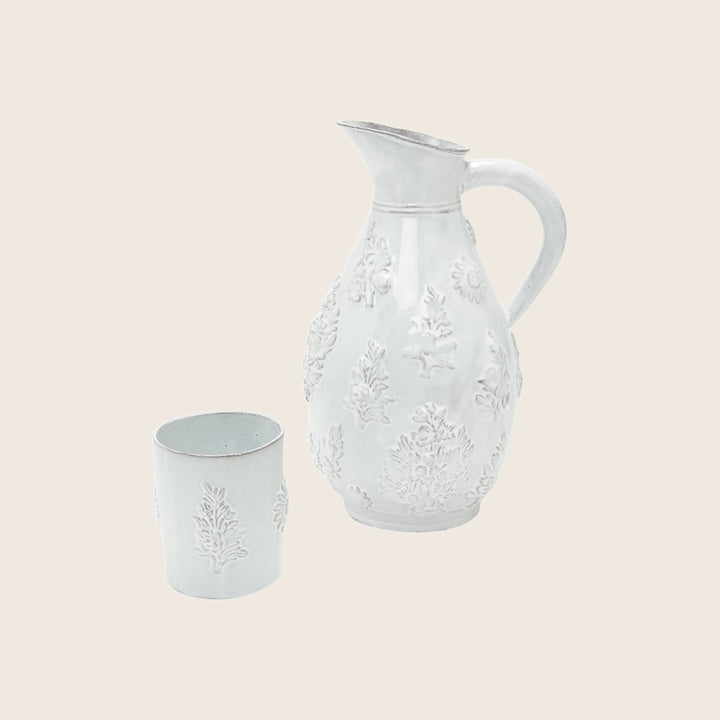 White ceramic pitcher and cup with botanical embossed design elements.