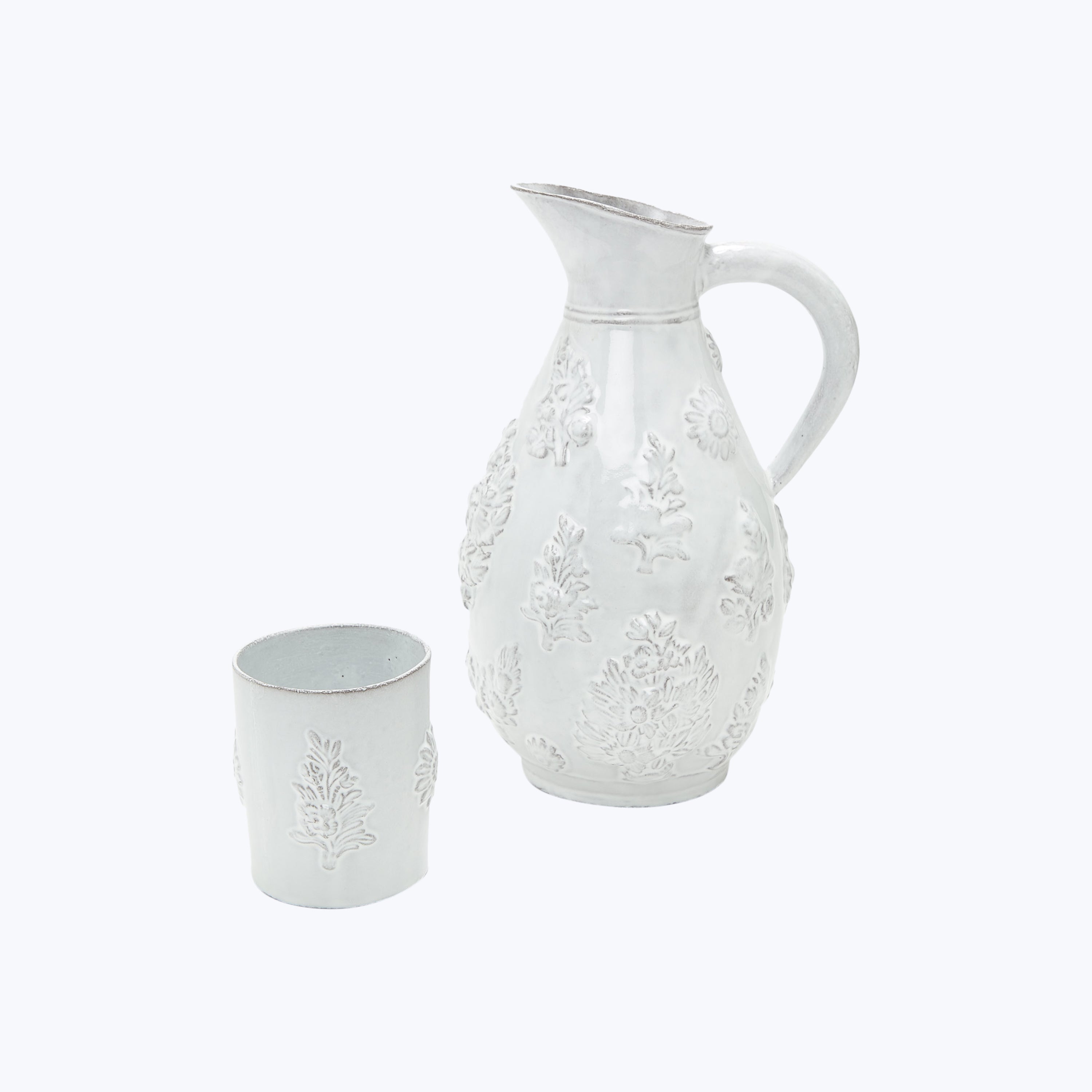 White ceramic pitcher and cup with botanical embossed design elements.