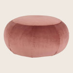Round, blush-pink pouf with plush velvet texture and stitched segments.
