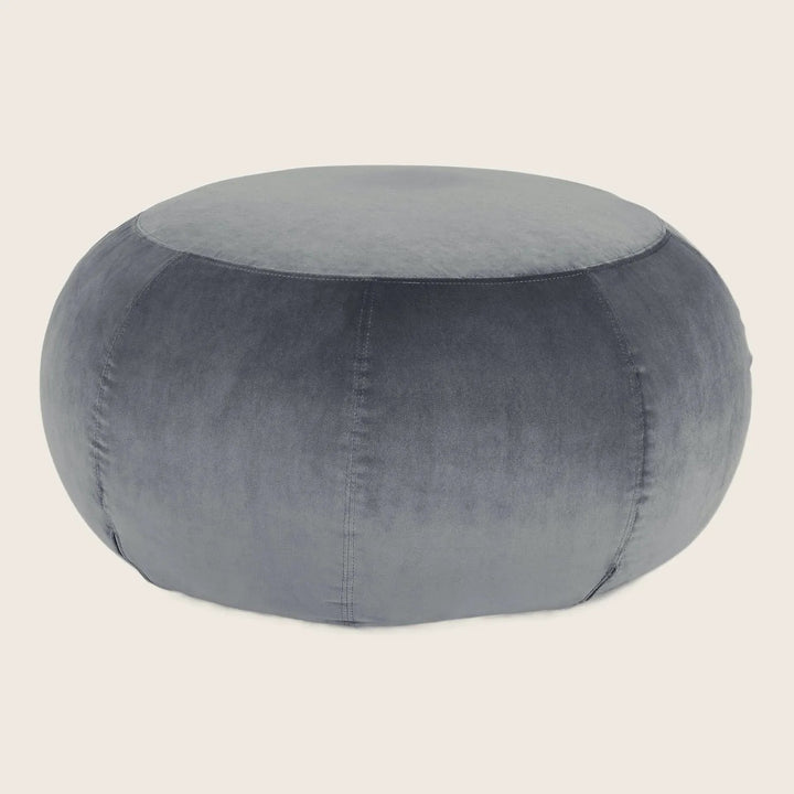 Grey velvet upholstered round pouf with visible stitching for seating