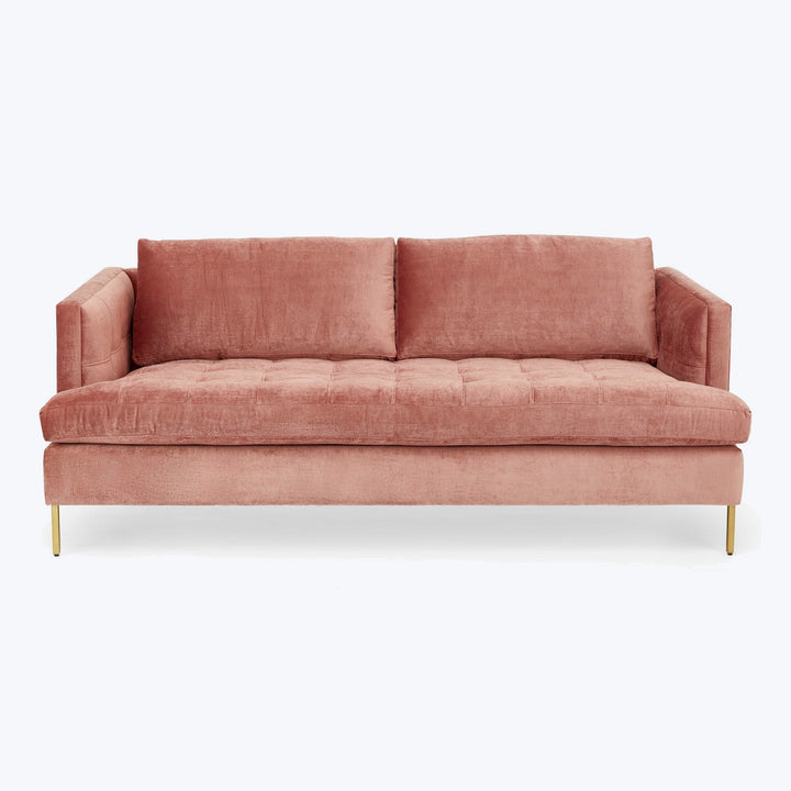 Modern velvet sofa in soft pink with tufted cushions on metal legs.