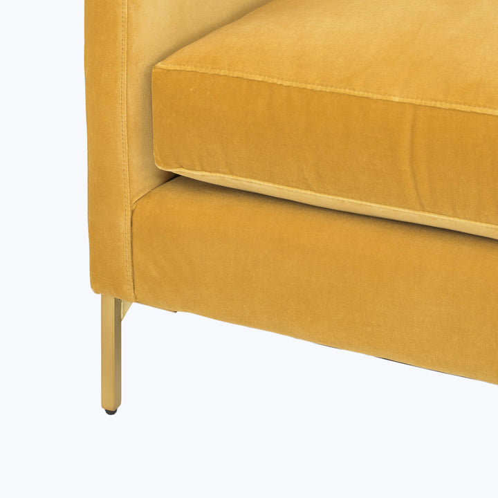Mustard-yellow velvet sofa with brass leg in close-up detail.
