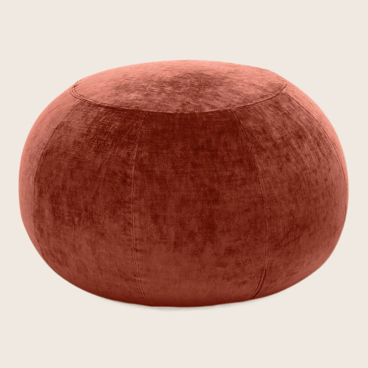 A burnt orange velvet pouf with elegant symmetrical design.