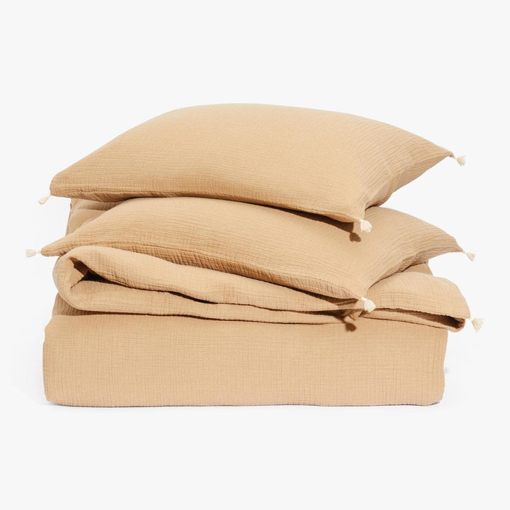 Neatly stacked beige bedding items with decorative tassels on pillows.