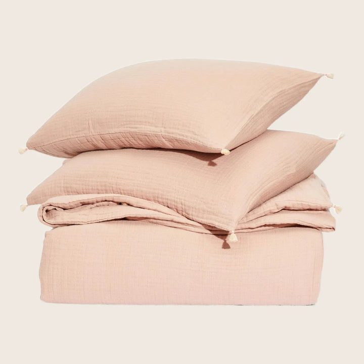 Cozy pink bedding set with tasselled pillows on white backdrop.