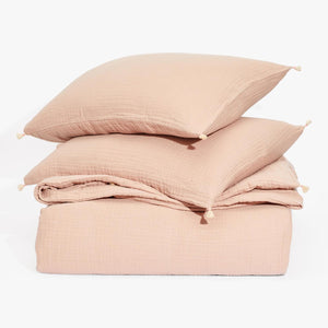 Cozy pink bedding set with tasselled pillows on white backdrop.