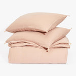 Cozy pink bedding set with tasselled pillows on white backdrop.