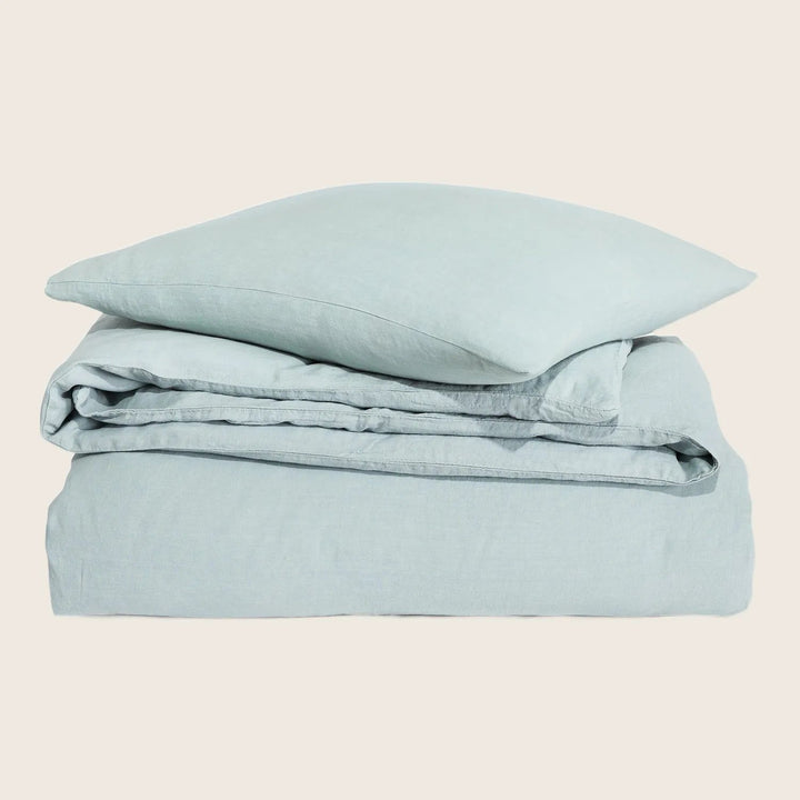 Neatly folded pale blue bed linens set on white background.