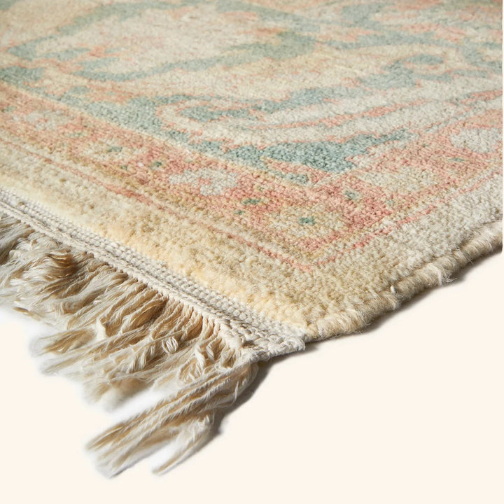 Close-up of handwoven rug with muted colors and fringe tassels.