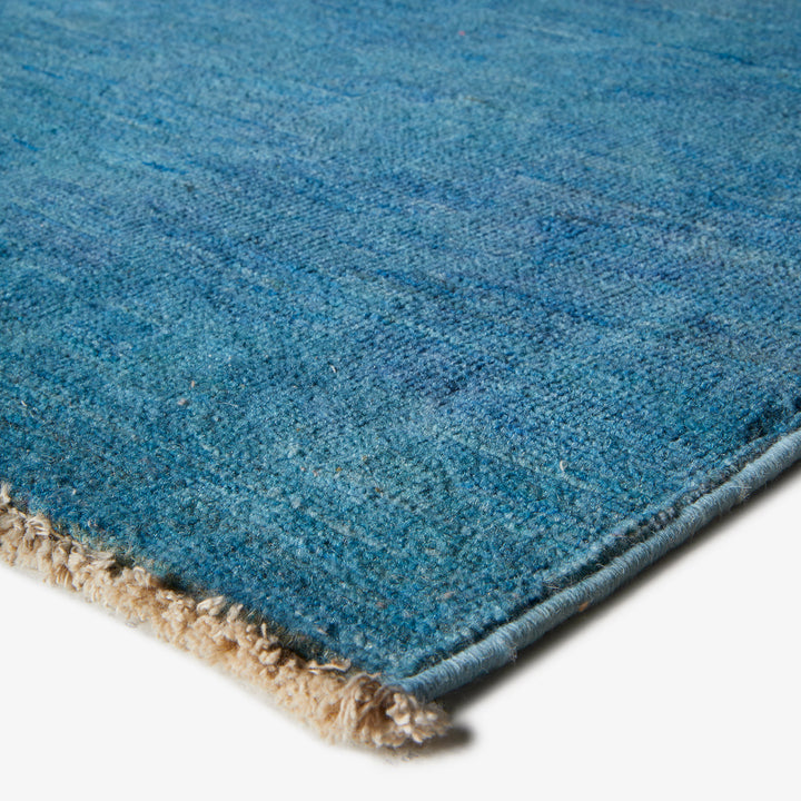 Close-up of blue rug with dense pile and fringe detail.