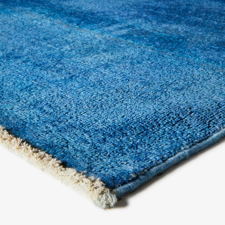 Close-up of textured blue rug with beige fringe, gradient pattern.
