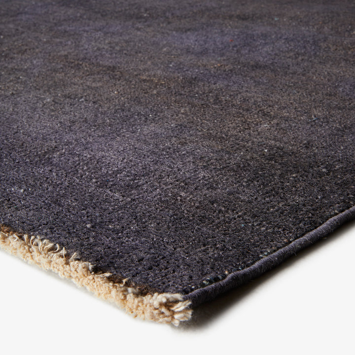Close-up of plush, dark-colored rug with gradient texture and stitching.